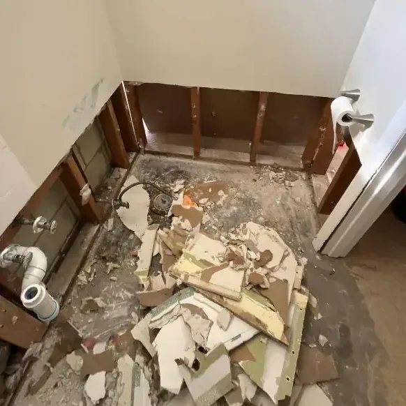 Opened bathroom walls with loose wallboard scattered across the floor