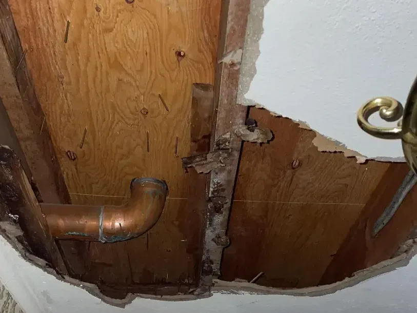 Ceiling opening revealing copper pipe and surrounding wood framing