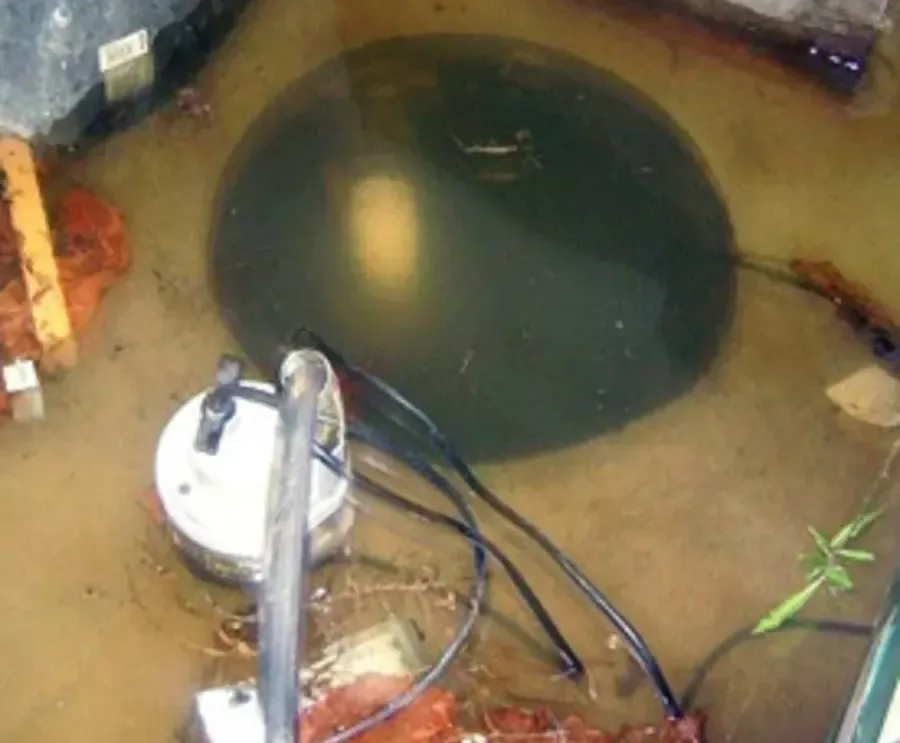 Pump and cables beside an open sump pit surrounded by water