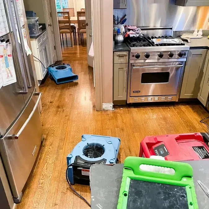 Air movers positioned across wet hardwood flooring inside a kitchen