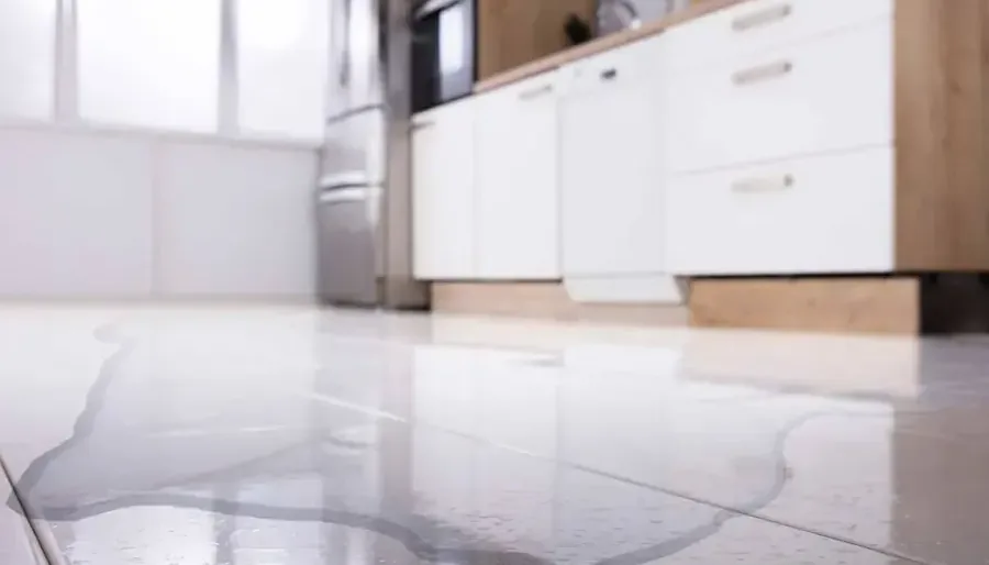 Water pooled across a kitchen floor in front of white cabinets and appliances