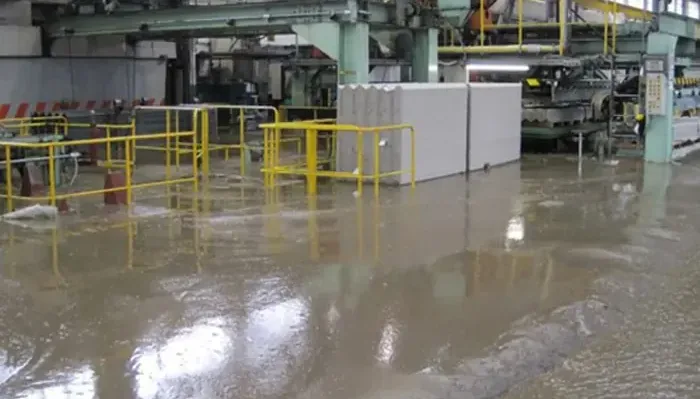 Standing water across an industrial floor beside yellow safety railings